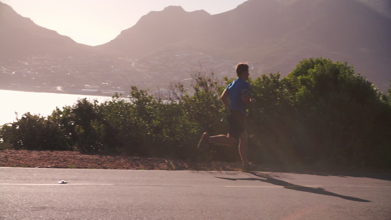 Young man running on an empty coastal road, slow motion