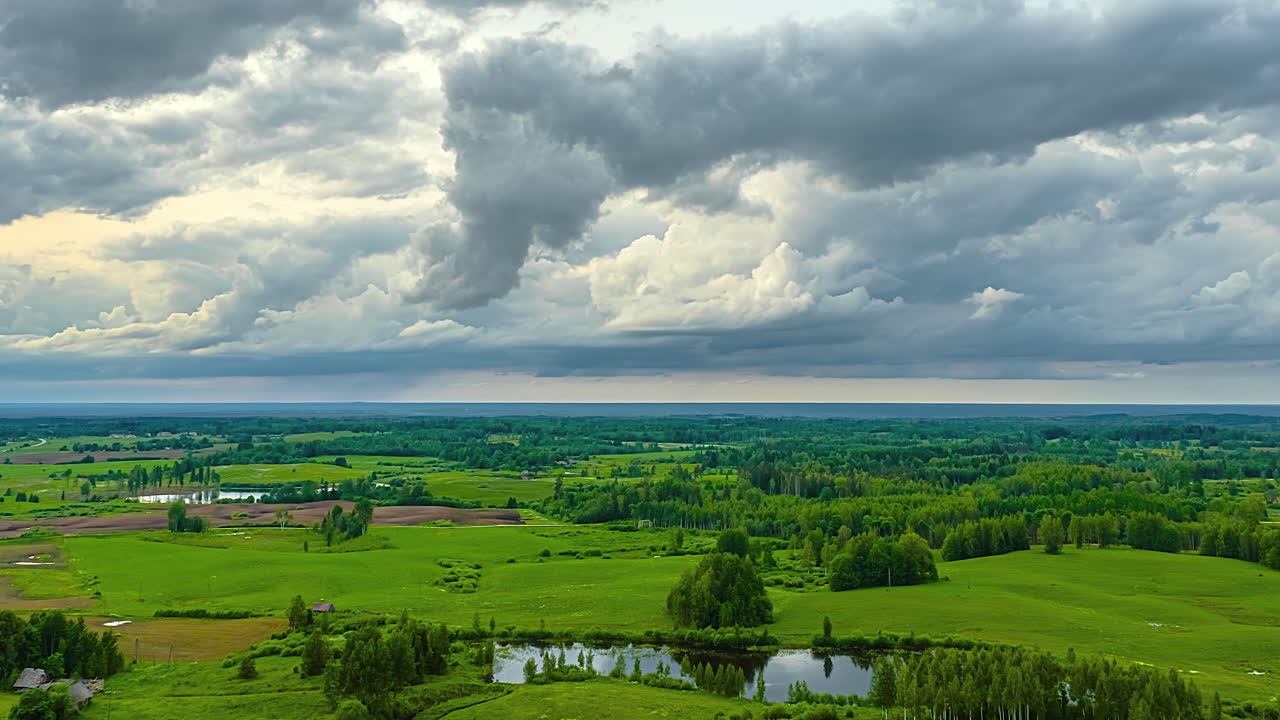 Aerial view of dense clouds sliding past over a green landscape. Time lapse