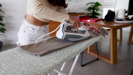 a woman irons pants on an ironing board in a bright, modern room with natural lighting