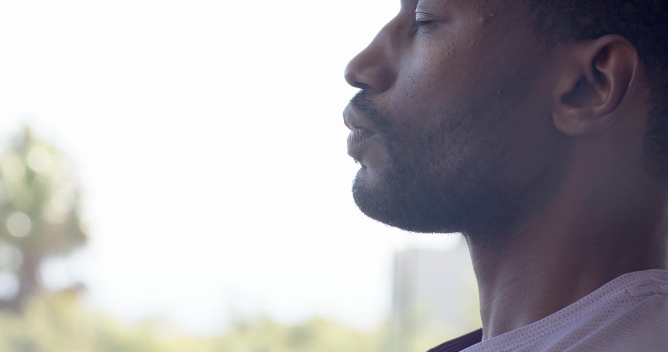 Man pressing hand to chest, lifting chin, practicing slow breathing by window, copy space