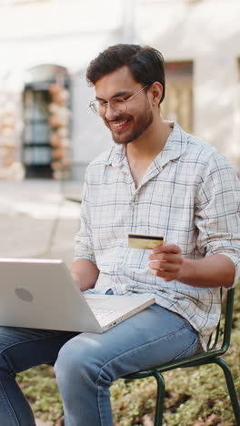 indian man using credit card laptop while transferring money purchases online shopping outdoors