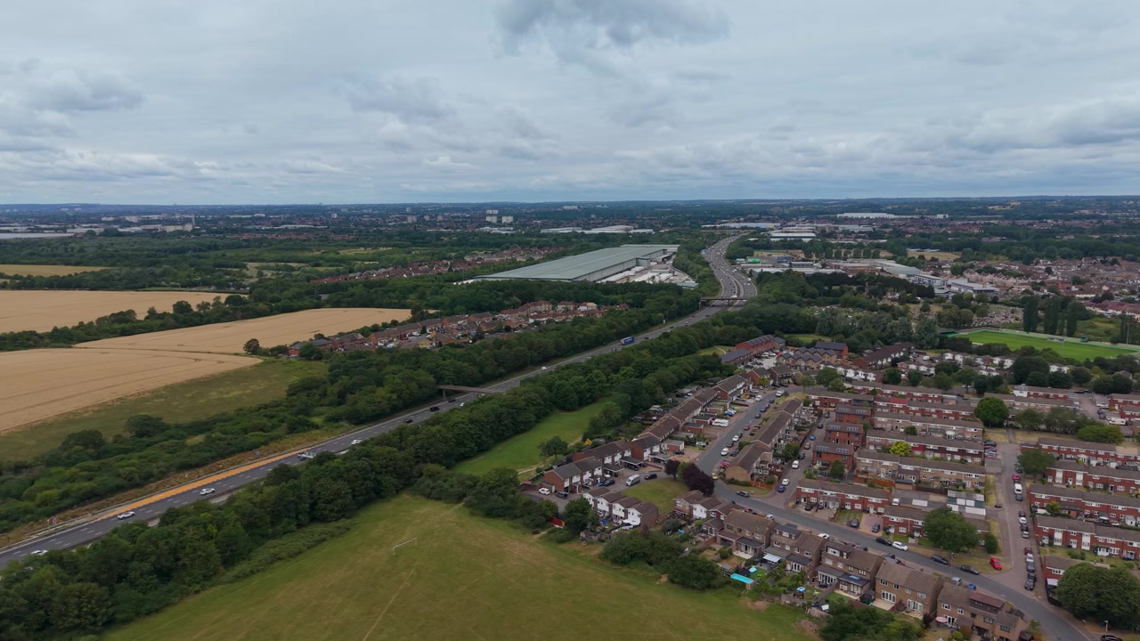 Orbita drone di Waltham Abbey verso la M25, con vista su Enfield. I complessi residenziali incorniciano il vasto Centro di Distribuzione Sainsbury's Waltham Point, evidenziando la scala ai margini della periferia.