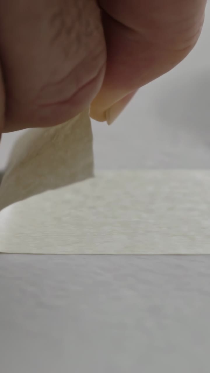 Vertical video: Entering finger and thumb pinching and removing cream tape on table showing back