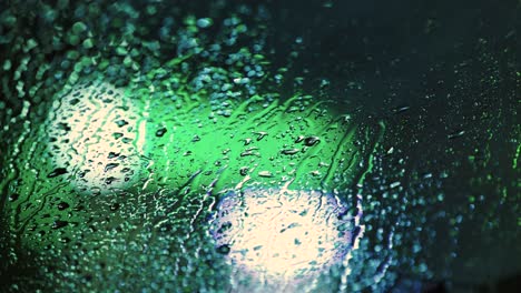 close up of rain water drops on car window glass with blurred traffic lights background at night.