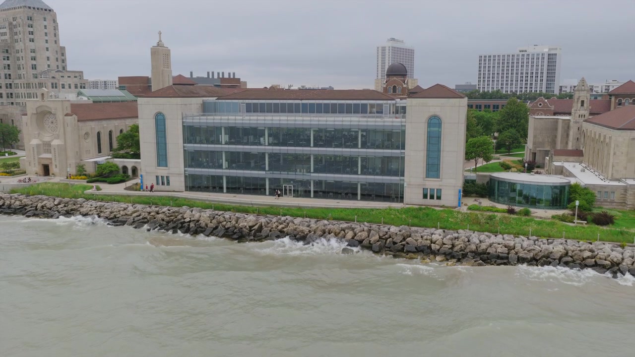 Ripresa con drone di un moderno edificio universitario con facciata in vetro a Chicago, lungo una costa rocciosa del Lago Michigan, con tetti a cupola nelle vicinanze