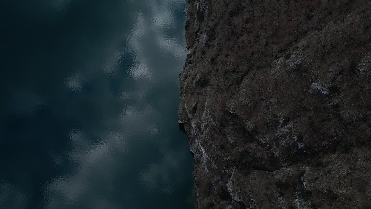 vista a vista de pájaro que muestra el agua en el borde del lago, encontrándose con un acantilado montañoso empinado, cubierto de vegetación silvestre