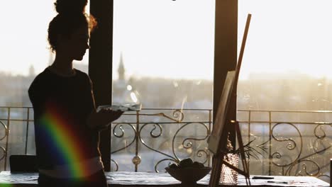 unrecognizable figure of female artist drawing on easel in an art studio with panoramic windows.