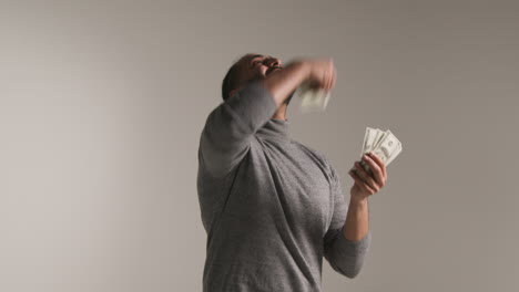 studio shot of excited man celebrating winning cash prize kissing and throwing handful of 100 dollar bills in the air