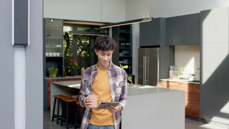 holding tablet and drinking coffee, teenage boy standing in modern kitchen