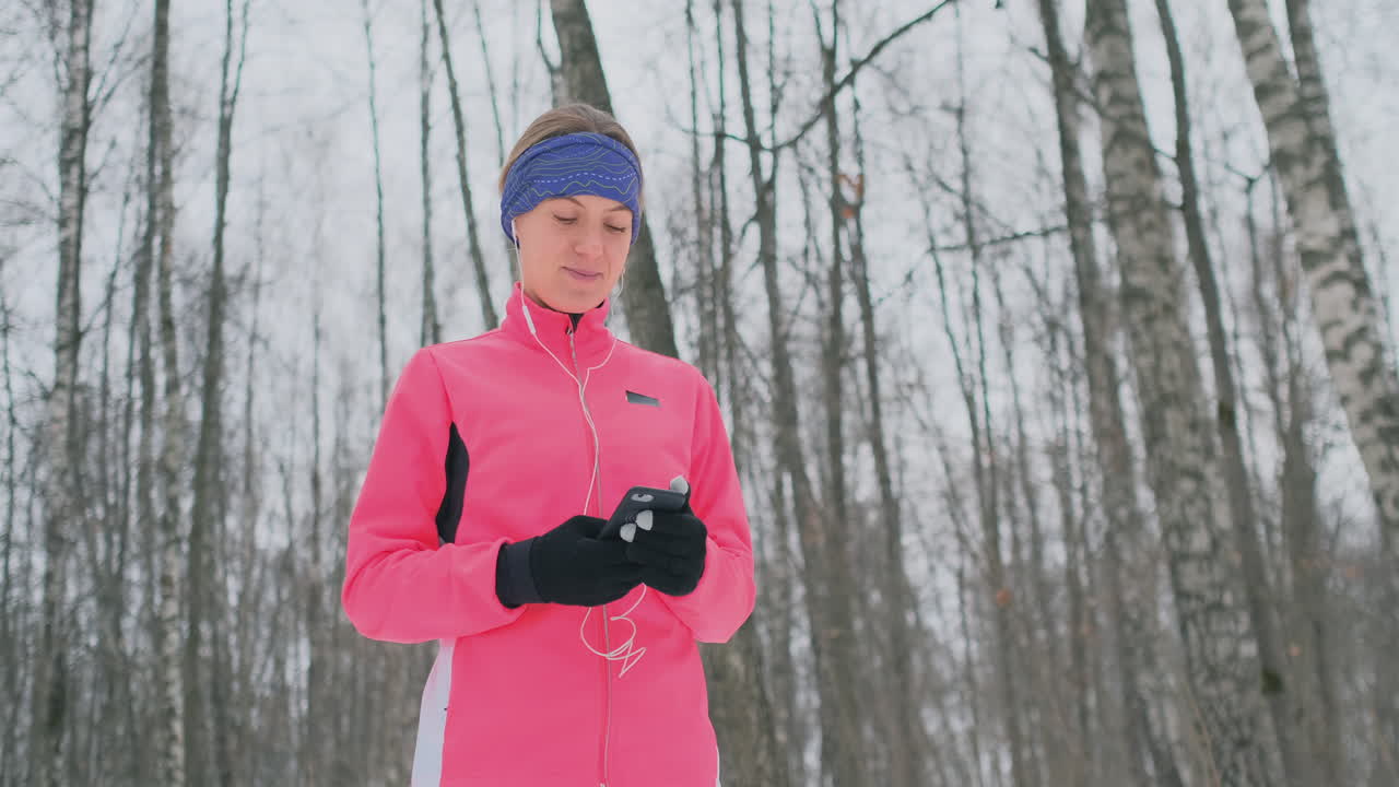A young woman on the morning jog holds in her hands a smartphone picks a music track for training. Winter run. Use modern gadgets and training applications
