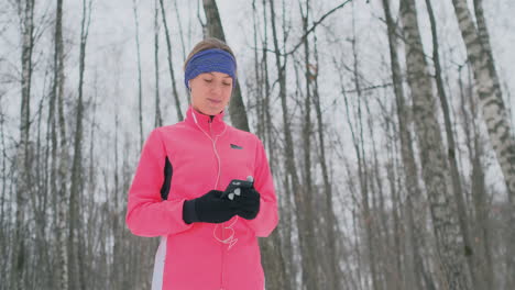 una joven que hace jogging por la mañana sostiene en sus manos un teléfono inteligente que elige una pista de música para entrenar. carrera de invierno. utilice dispositivos y aplicaciones de formación modernos.