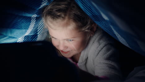 Fröhliches-Kleines-Mädchen,-Das-Unter-Einer-Decke-Einen-Digitalen-Tablet-Computer-Benutzt,-Das-Lernen-Auf-Touchscreen-Technologie-Genießt,-Spiele-Spielt-Und-Vor-Dem-Schlafengehen-Spaß-Hat