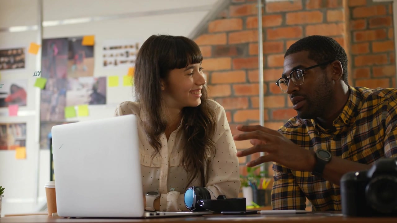Man starting pitch with broad gestures, woman leaning toward laptop, callouts highlighting design