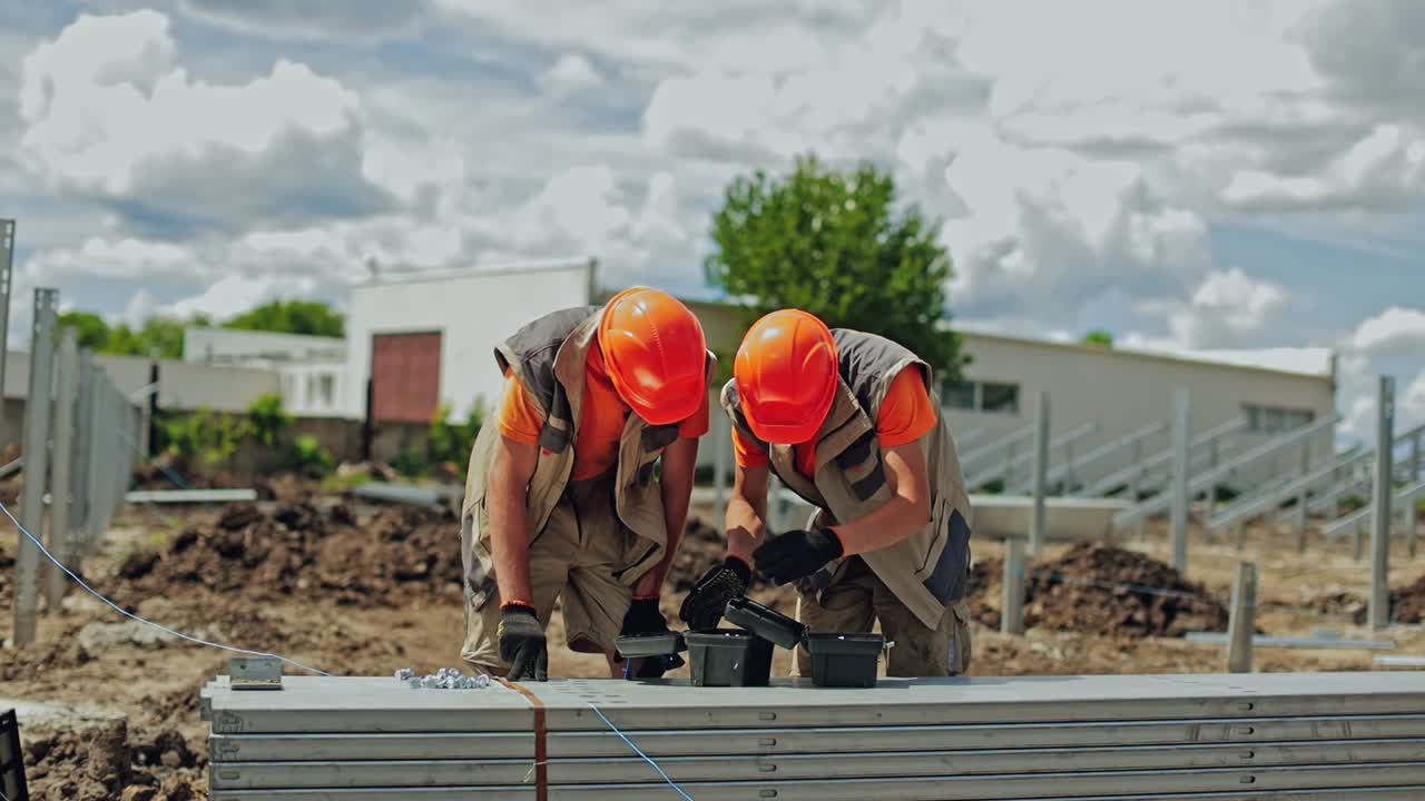 Solar plant construction. Two workers in orange helmets prepare instruments for building solar panels. Engineers installing metal basis for future solar power plant.