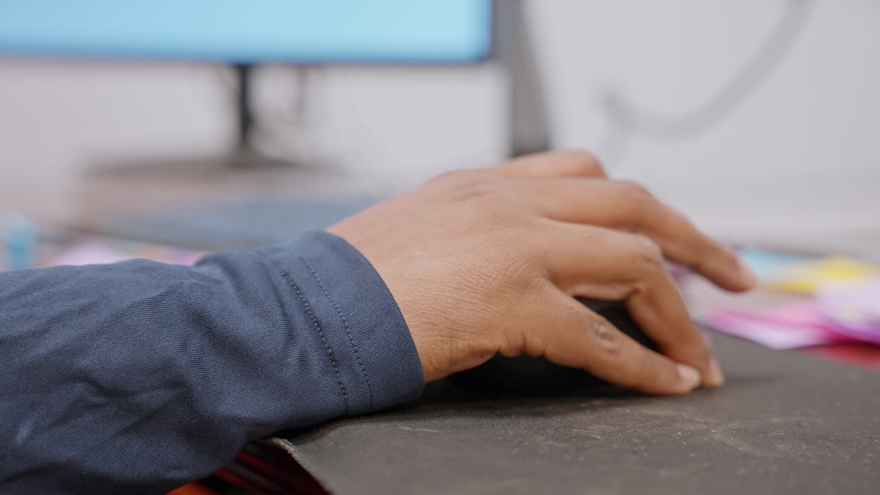 Person using computer mouse lifting fingers slightly at desk in modern office workspace