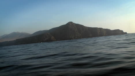 A-boat-passes-through-the-water-with-other-boats-and-mountains-in-the-distance