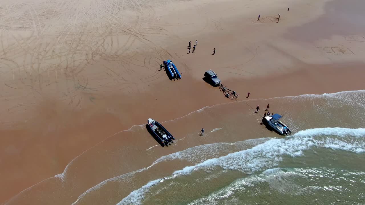 뜨거운 모래사장으로 굴러 들어갈 때 파도에서 보트를 싣는 사람들의 매끄러운 높은 각도의 공중 전망