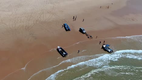 a smooth high angle aerial view of people loading a boat out of the waves as they roll into the hot sandy beach