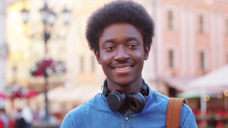 Gros plan sur un homme afro-américain regardant la caméra et souriant dans la rue.