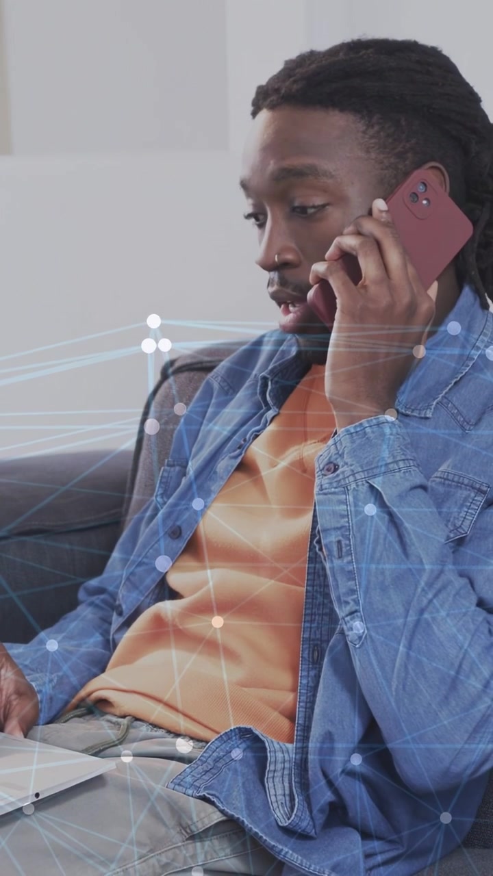 Vertical video: Man holding red phone while swiping laptop, network overlay guiding work typing