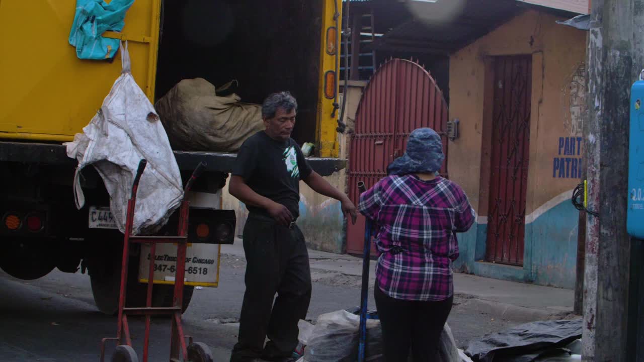 People loading and unloading waste from a truck in a city street