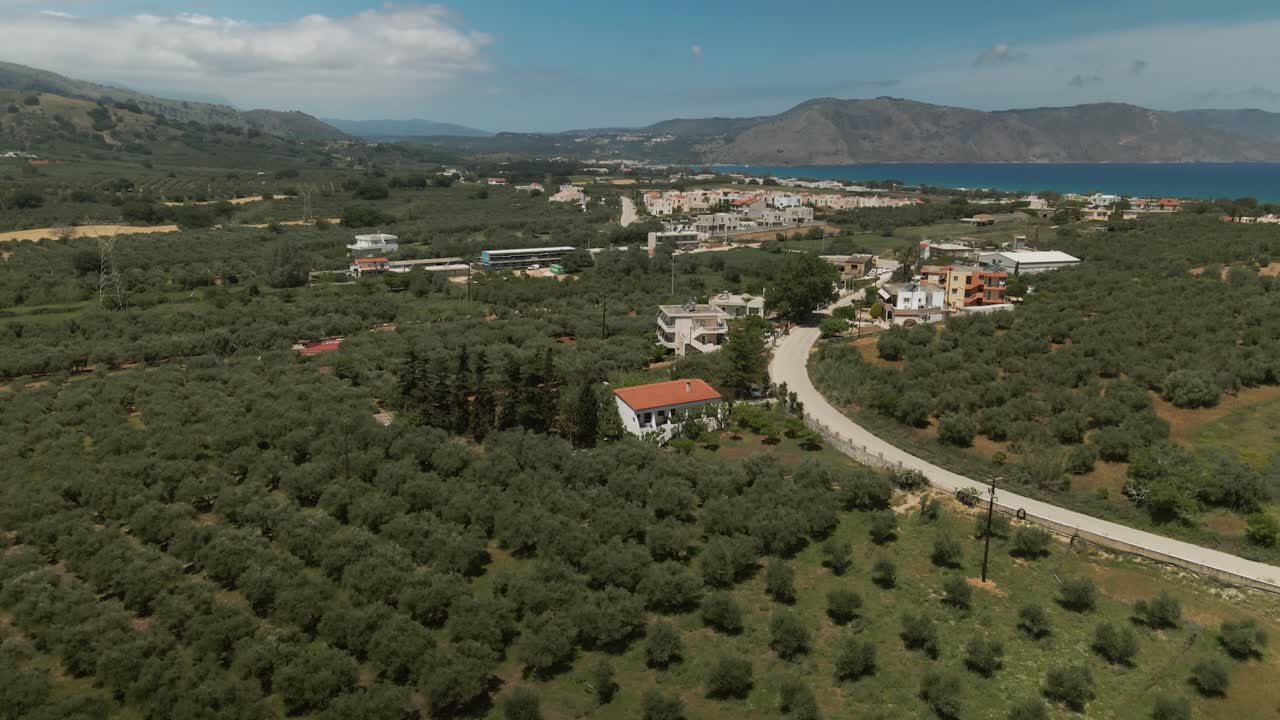 Overhead view of cultivated olive fields and scattered village houses near coastal hills in the Asprouliani region of Crete, Greece