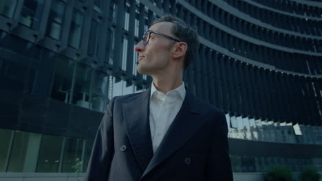 handsome caucasian man in suit standing outdoors at financial district looking around at buildings