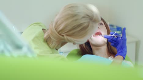 젊은 여성의 마취를 하는 치과의사. 입 거울을 사용하는 여성 치과의사