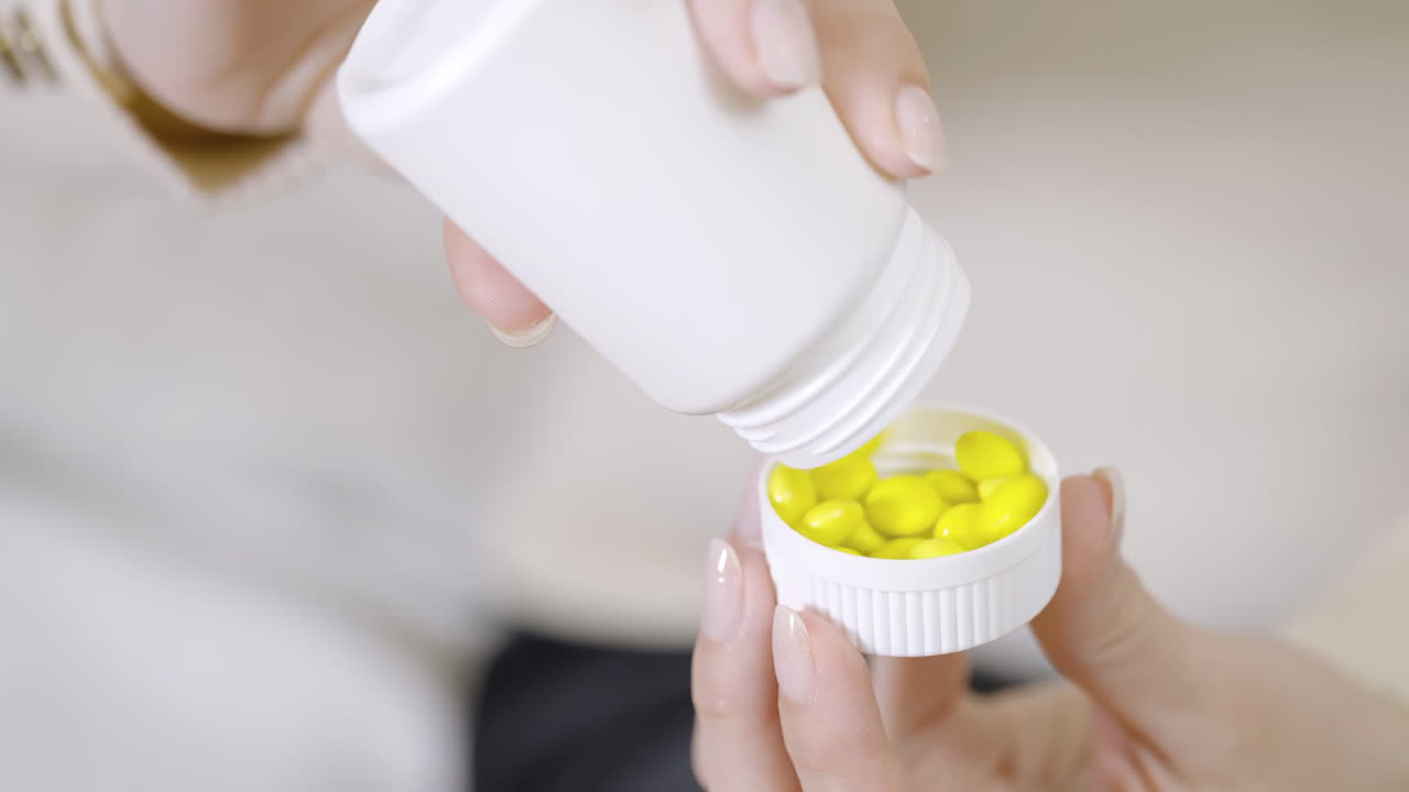 People young woman pouring yellow transparent capsules from a white bottle into her palm for a daily dose of vitamins, folic preconception drug bottle or weight loss diet drug, body skin health care