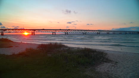 Filmische-Luftlandschaft-Mackinaw-Bridge-Leuchtturm-Michigan-Sonnenuntergang-Abenddämmerung-Lila-Rosa-Atemberaubende-Landschaft-Der-Großen-Seen-Hochsommer-Im-Norden-Petoskey-Harbour-Springs-Autos-Brücke-überqueren-Vögel-Schwenk-Nach-Links