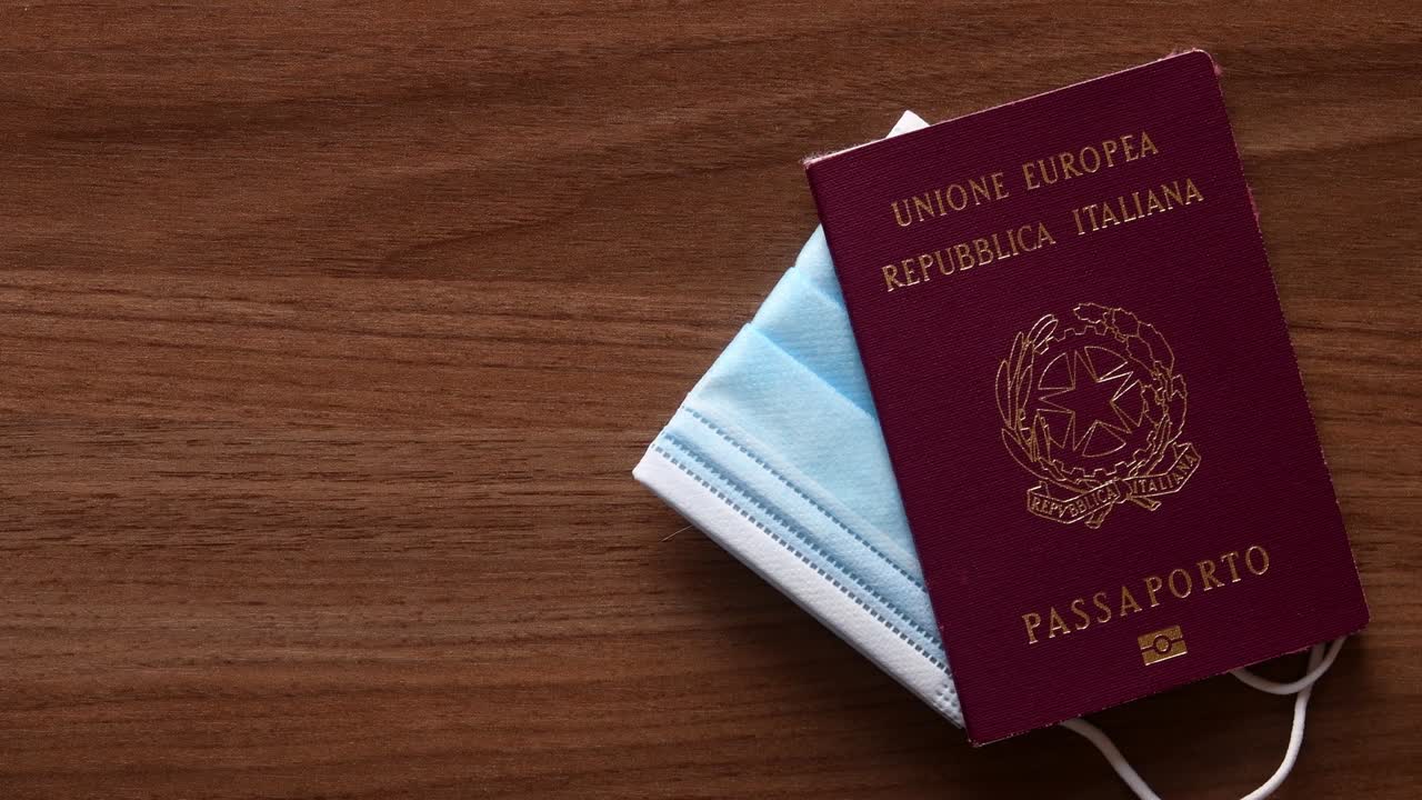 Surgical mask, passport and smartphone (with green screen and tracking marks) tossed on wooden table