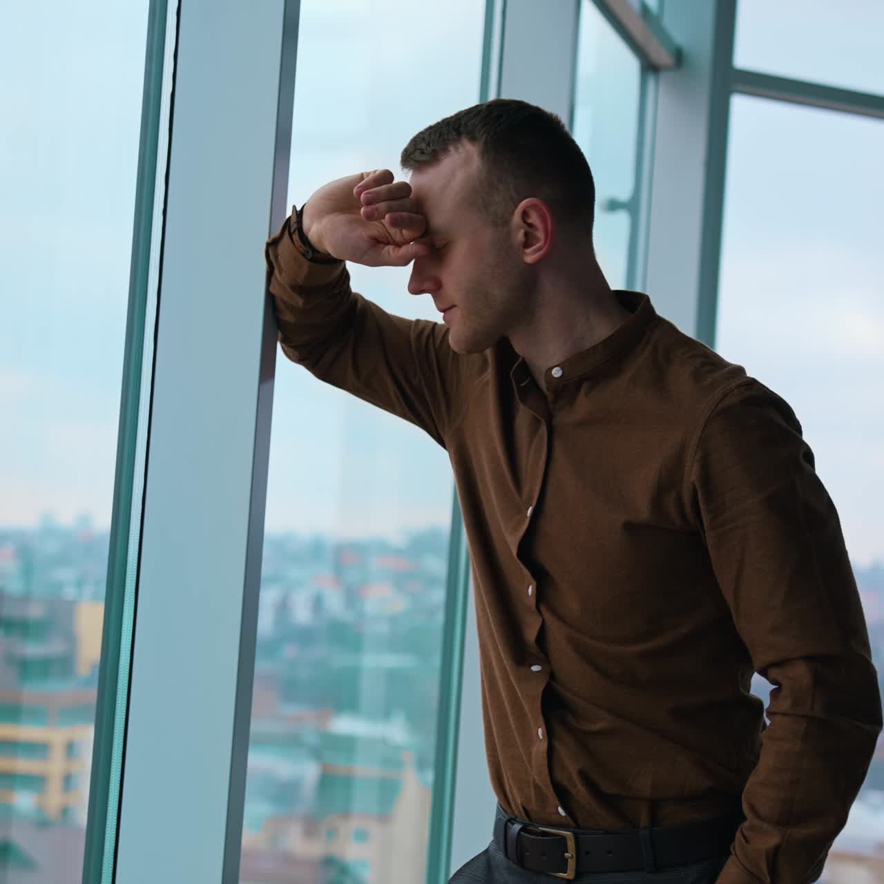 Full-length portrait of a businessman indoors. Tired young man walking along the office and stands by the large window with city view background