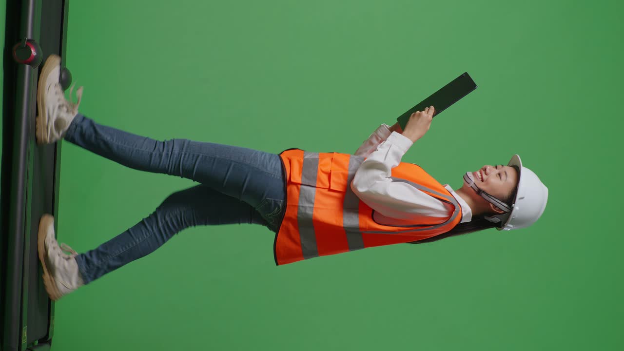 녹색 화면 배경 스튜디오에서 는 동안 태블릿을 사용하여 안전 헬을 착용한 아시아 여성 엔지니어의 전체 몸의 측면 뷰