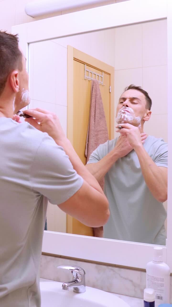 Man shaving his beard in bathroom mirror