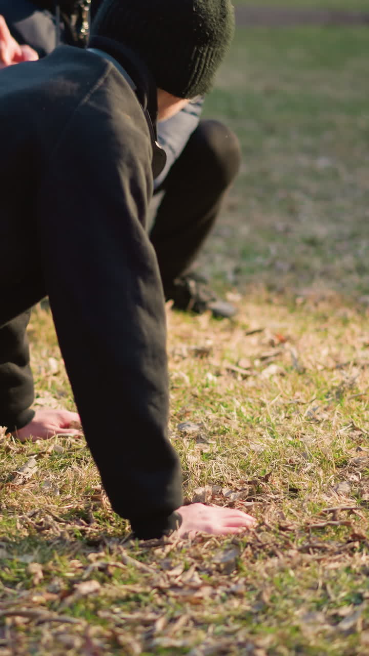 A coach supervising and counting the number of push-ups performed by a young boy dressed in black on a grassy field illuminated by light