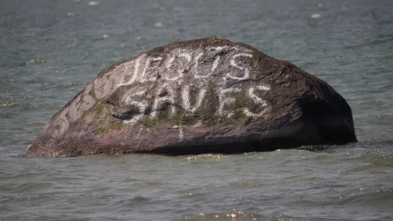 Weathered stone, coastal painted message, Christian faith, slow motion