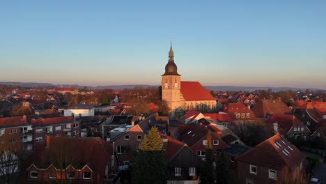 aerial approaching shot of historic catholic church of nottuln, germany. golden sunset time over small german town. wide shot. sandstone tower in historic city, europe.