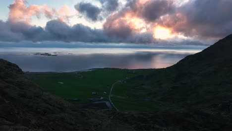 cliffs and ridge of mountain mannen passed by drone, revealing utakleiv beach, ocean and pink clouds