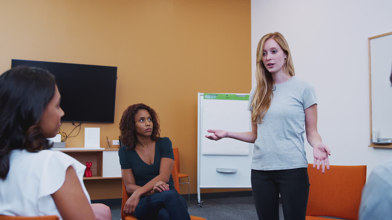 mujer de pie dirigiéndose a un grupo de hombres y mujeres en una reunión de terapia de grupo de salud mental
