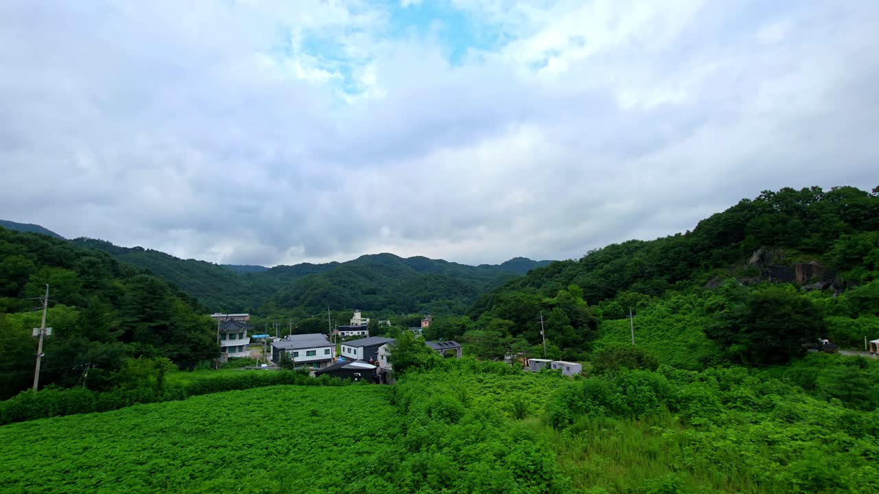 Scenic rural Gapyeong landscape seen in motion, showcasing green fields, local homes, forested mountains and shifting clouds