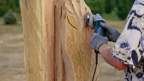 Hands in gloves hold the grinding tool working with wood. Process of wooden sculpture creation.