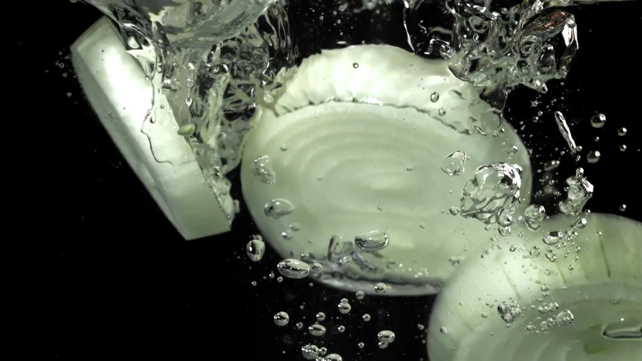 Sliced White Onions Falling into Water with Bubbles on Black Background