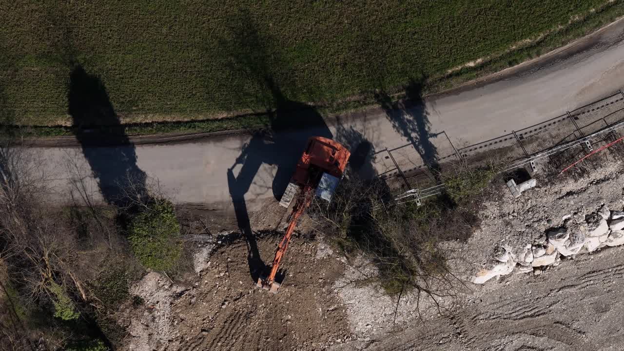 Drone view from above showing excavator digging drainage trench along road during maintenance works