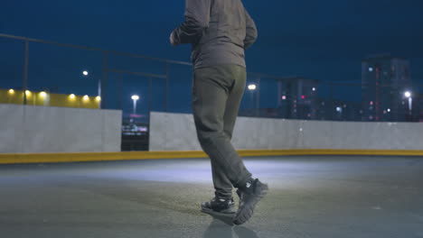 partial view of athlete kicking soccer ball toward goal post during night training session on urban outdoor field, city lights and buildings as the ball bounces out of the post