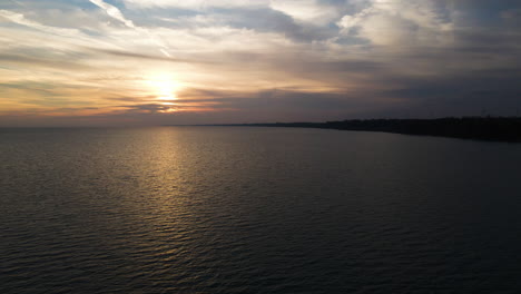 Drone-reverse-pullback-above-lake-with-ripples-reflecting-sunlight-rays-at-dusk