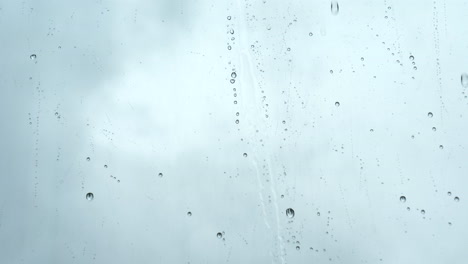 Close-up-of-water-rain-drops,-falling-onto-a-window-on-gray-cloudy-day