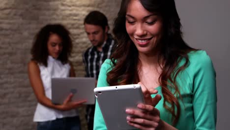 mujer usando una tableta digital mientras sus colegas discuten con una computadora portátil en la oficina