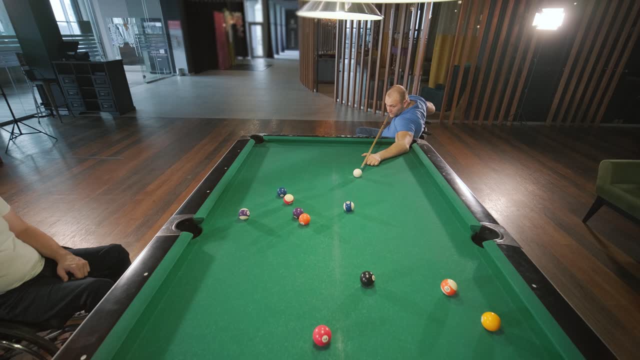 Adult men with disabilities in a wheelchair play billiards in the club