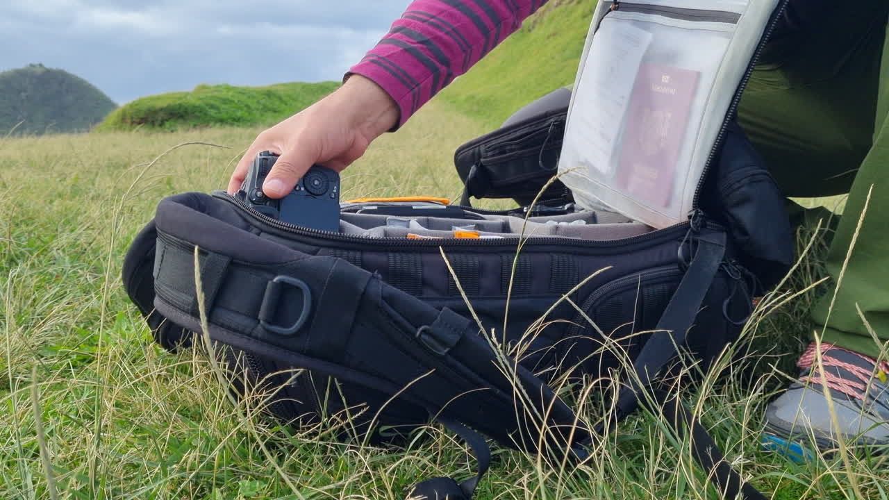 Photographer taking a professional digital camera out of a backpack while sitting on grassy hills