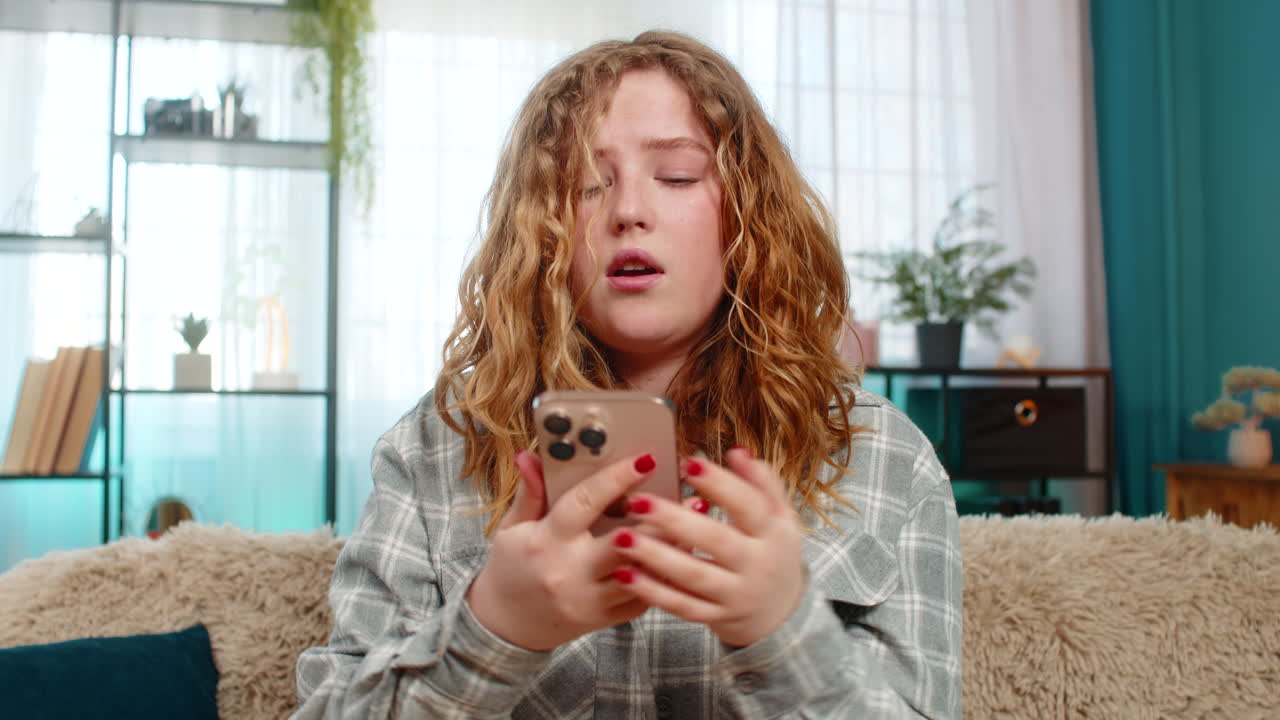 Young woman sitting on sofa holding mobile phone looking sad disappointed after receiving bad news